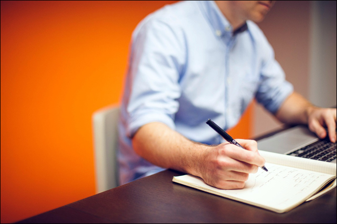 Image of man working on a laptop and writing on a notebook.