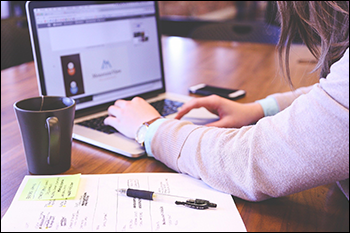 Content Documentation - Woman typing on laptop with notes.